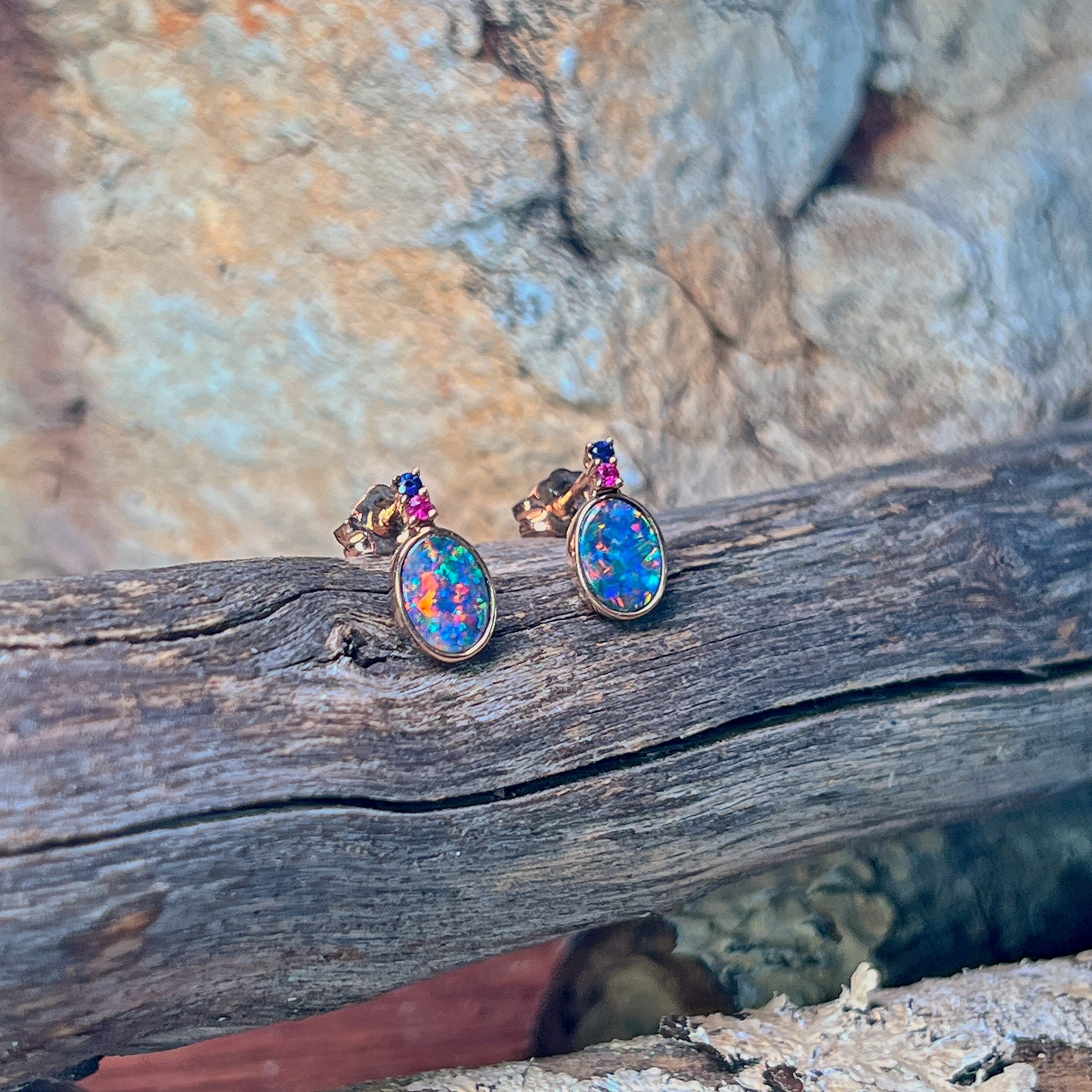 Oval opal doublet studs in rose gold with gemstone accents, angled on driftwood