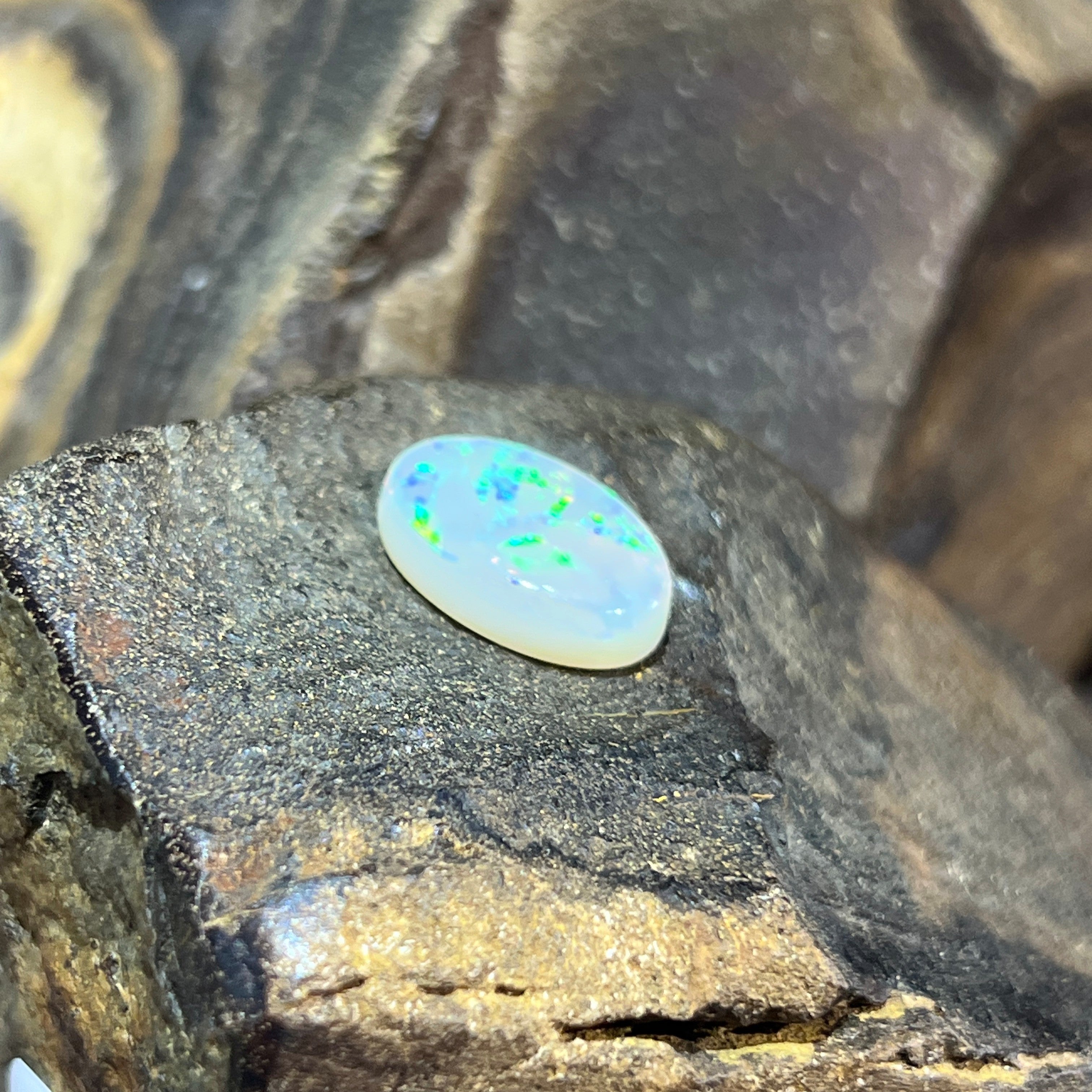 Angled view of the 5.56ct white opal, green sparkle scattered across the dome
