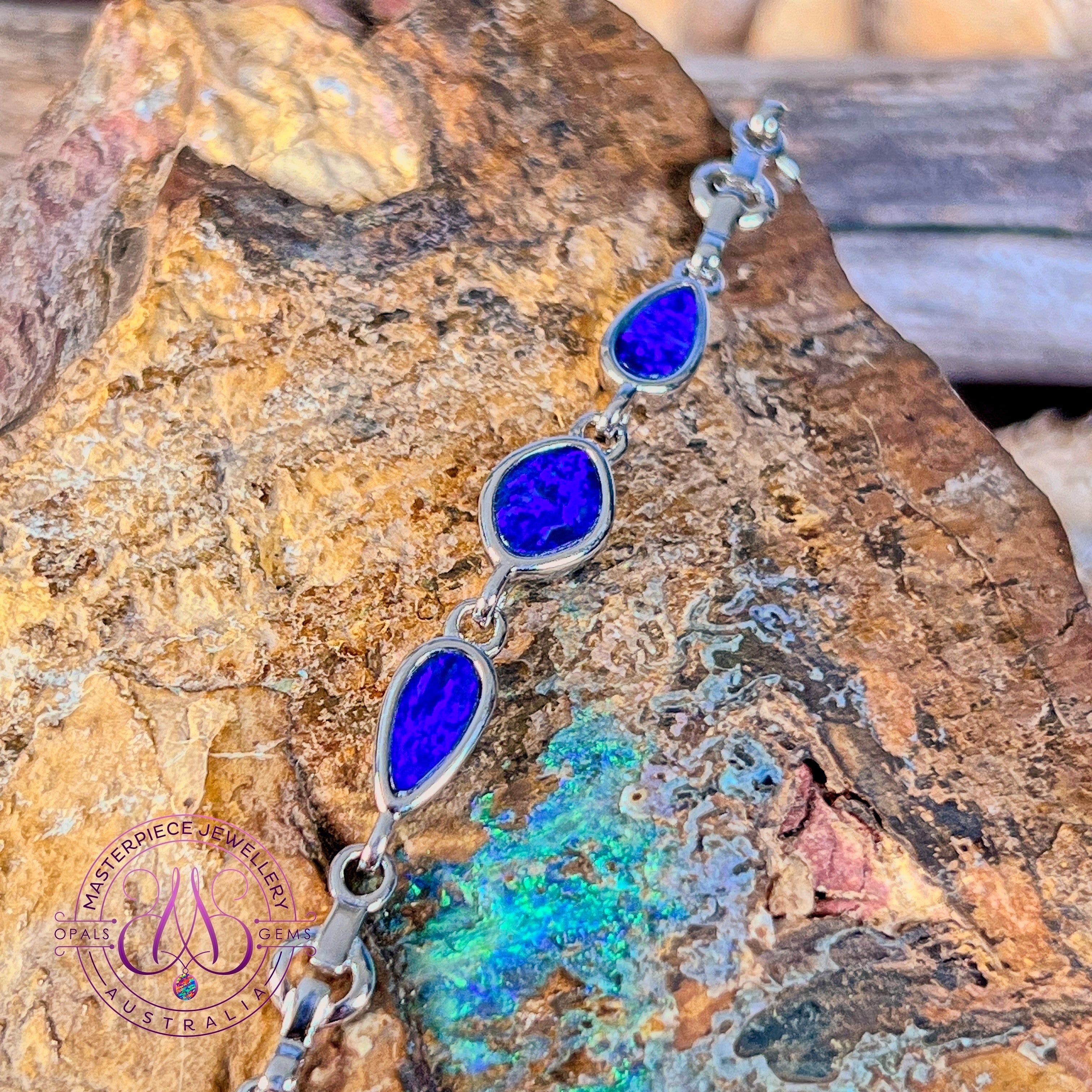 Sterling silver bracelet with three opal doublets against a weathered rock face, showing the linked stones