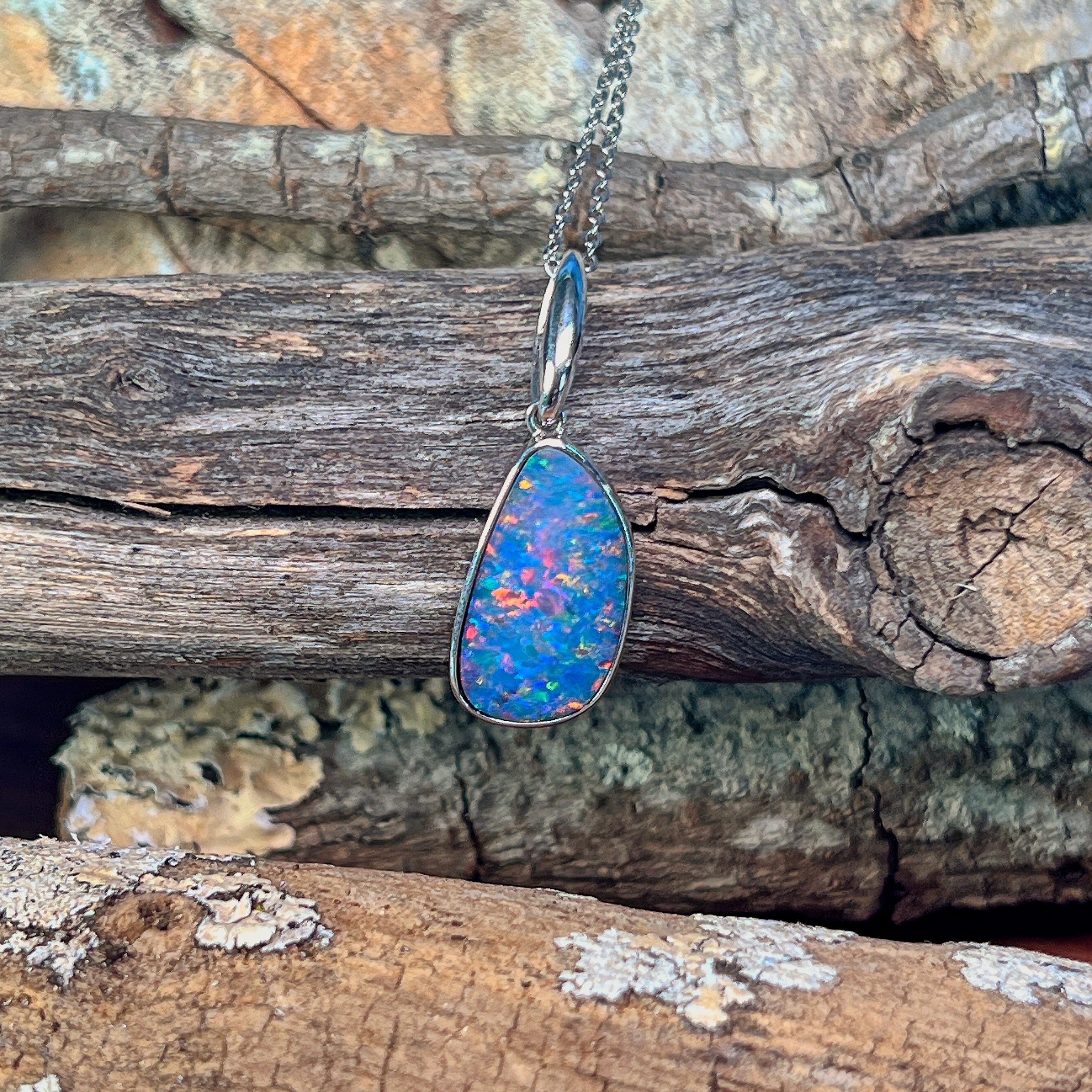Sterling silver opal doublet pendant with red flash hanging against weathered driftwood