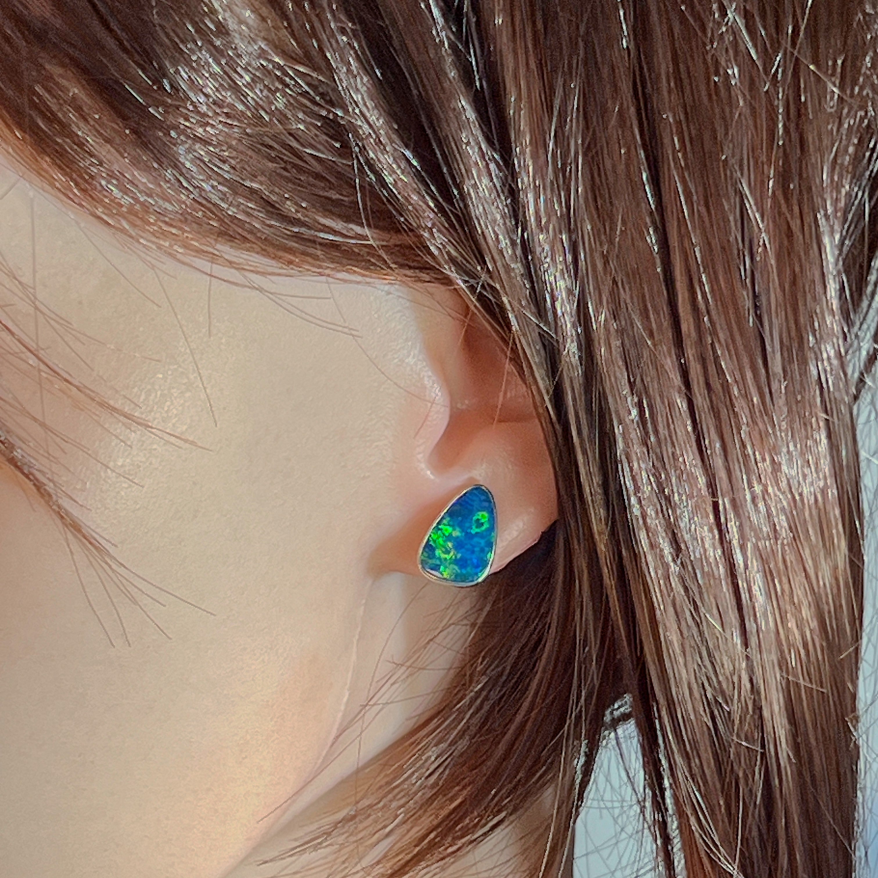 Blue-green opal doublet stud earring worn on the ear, close view of the silver bezel