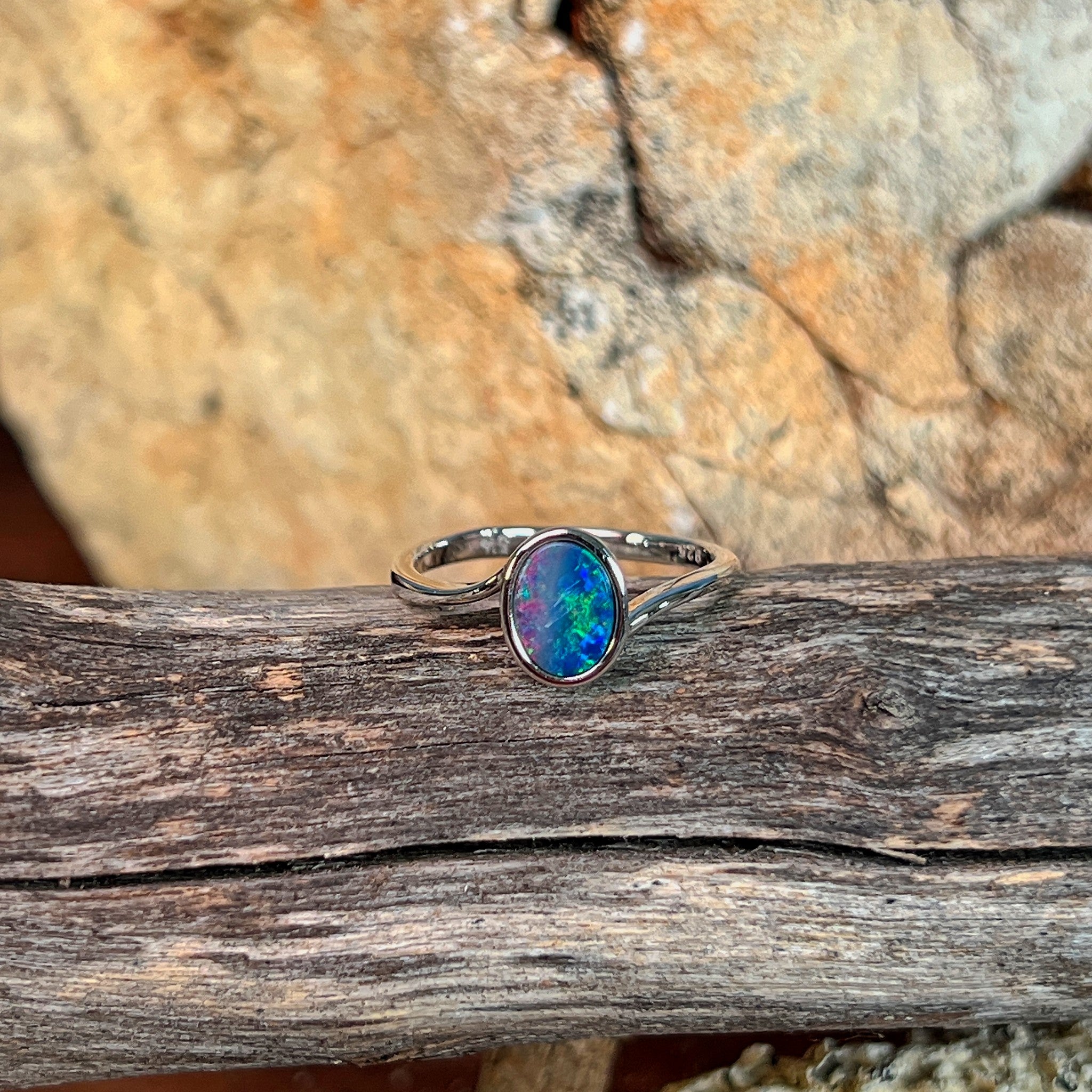 Oval opal doublet solitaire ring in silver resting on weathered driftwood