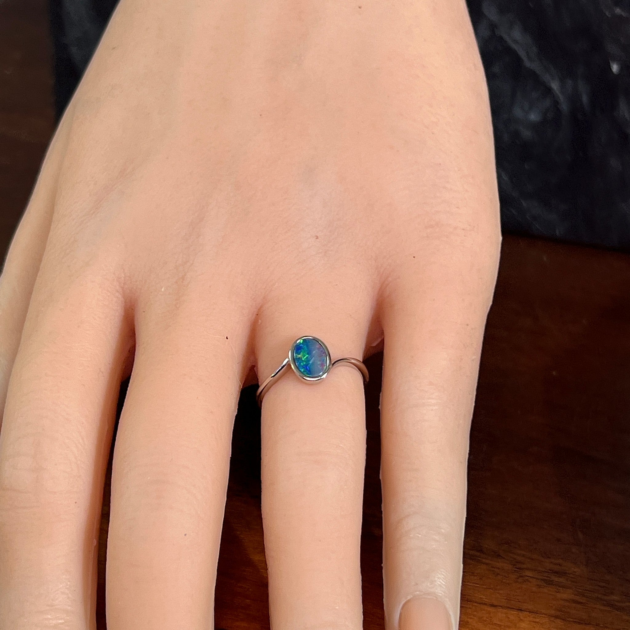 Oval opal doublet solitaire ring in silver worn on the hand, viewed across the fingers