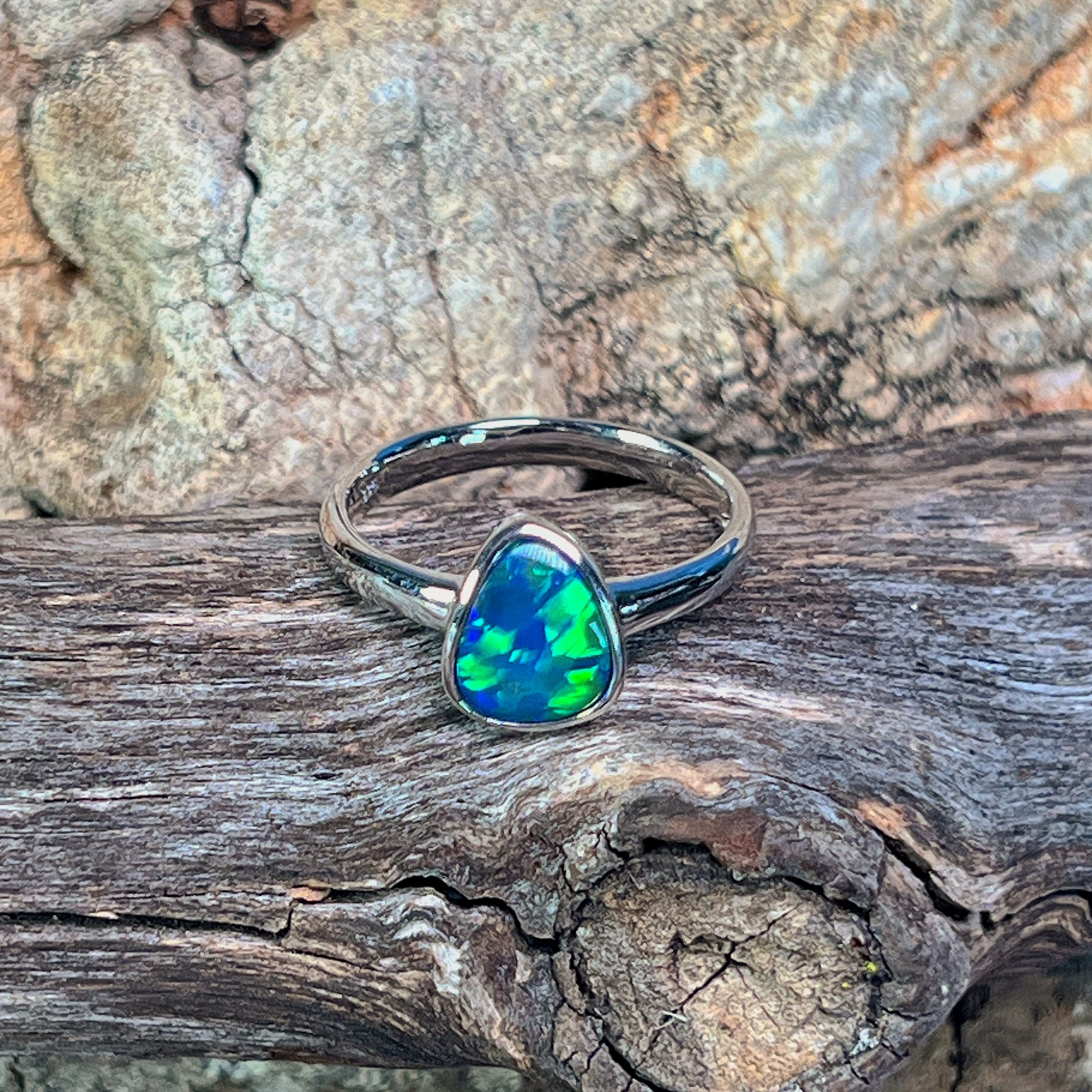 Sterling silver pear opal doublet solitaire ring angled against driftwood