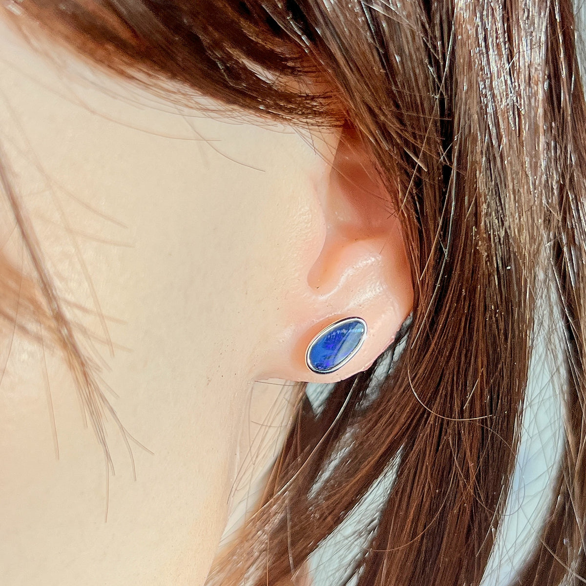 Australian opal doublet earrings worn on the ear, blue and black play-of-colour