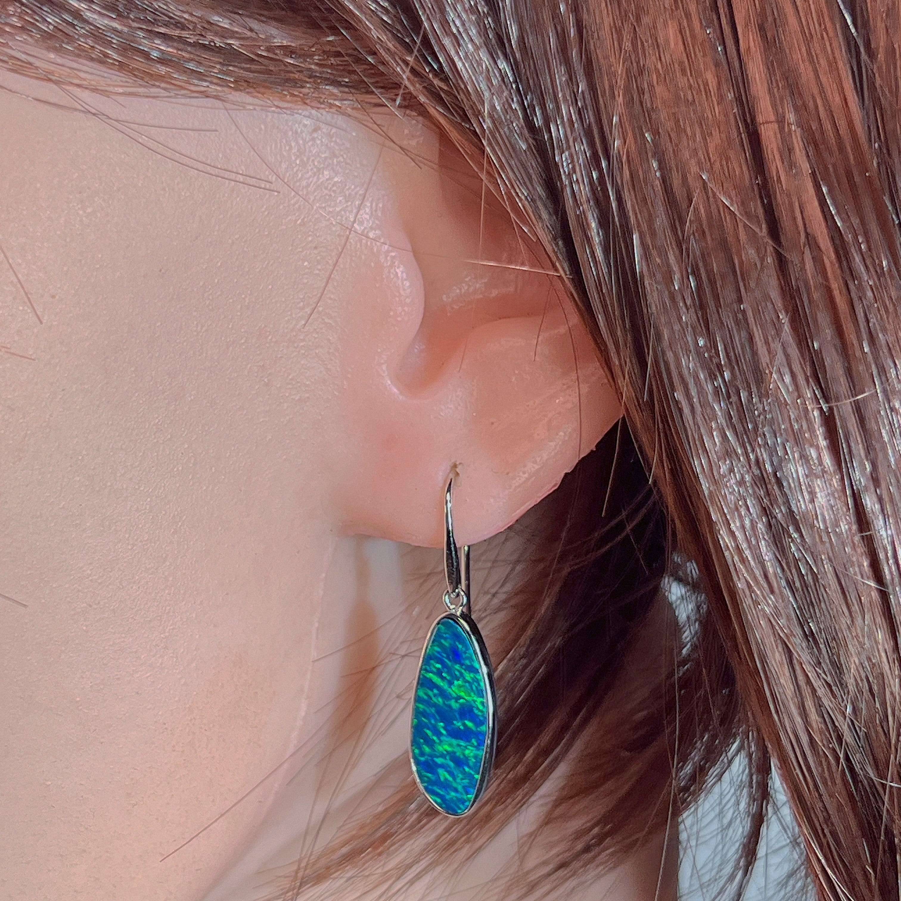 White gold opal doublet drop earring worn on the ear, showing its length on the earlobe