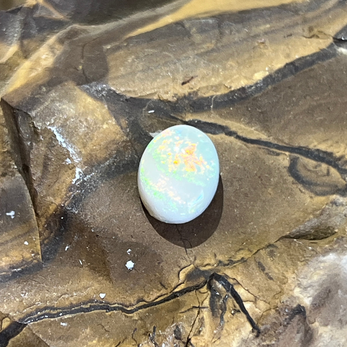 Australian white opal close up, gold and orange play of colour across the upper half