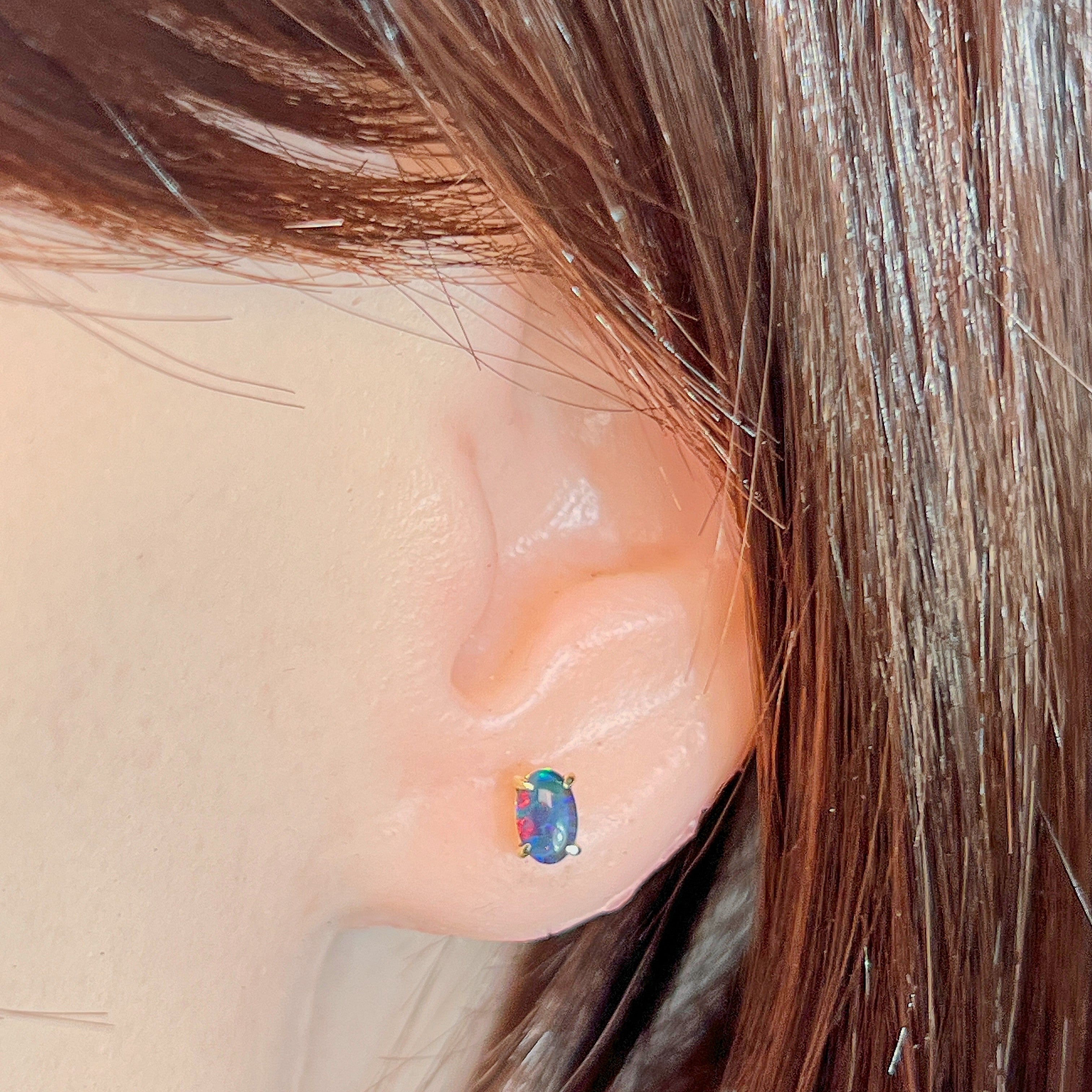 Small oval opal triplet stud earring worn on the ear beneath loose hair