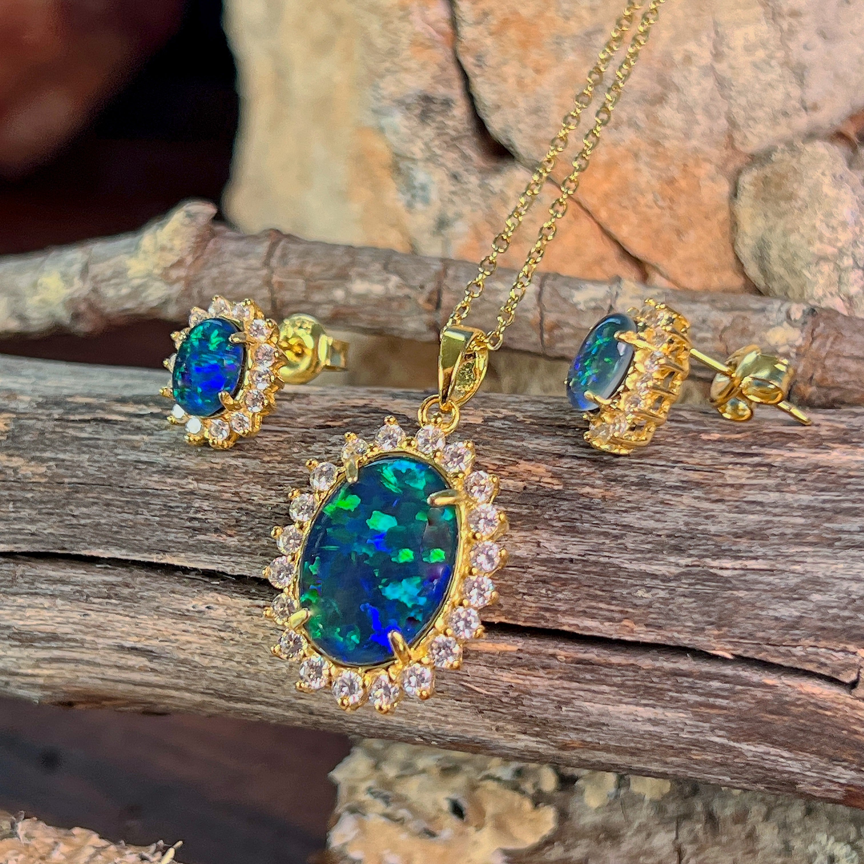 Halo-set opal triplet jewellery set in yellow gold-plated silver, viewed on driftwood