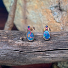 Rose gold oval opal doublet studs with ruby and sapphire accents on weathered driftwood