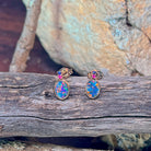 Pair of 14kt rose gold opal doublet stud earrings resting on driftwood and sandstone