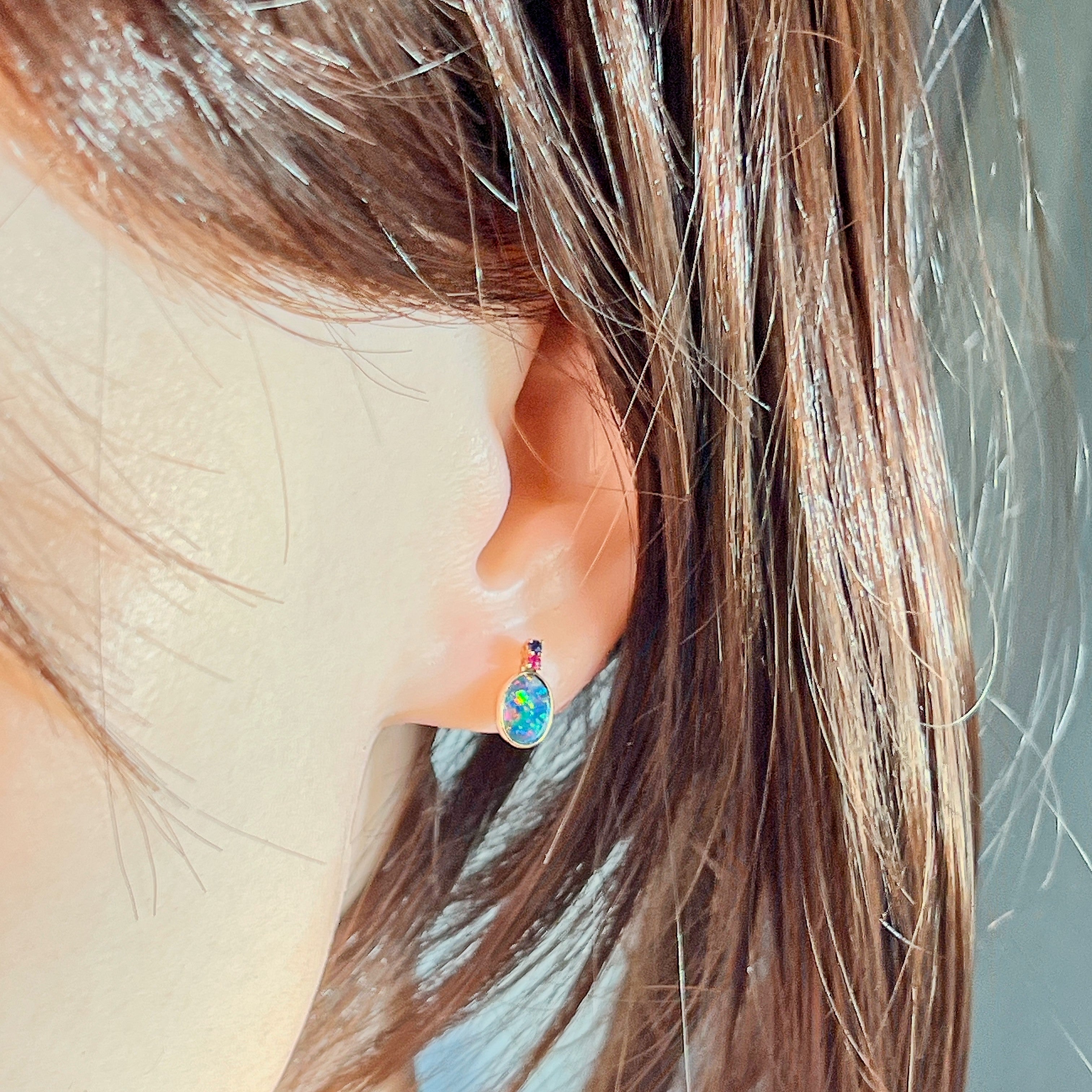Opal doublet stud with ruby and sapphire accents worn on the ear, side profile view