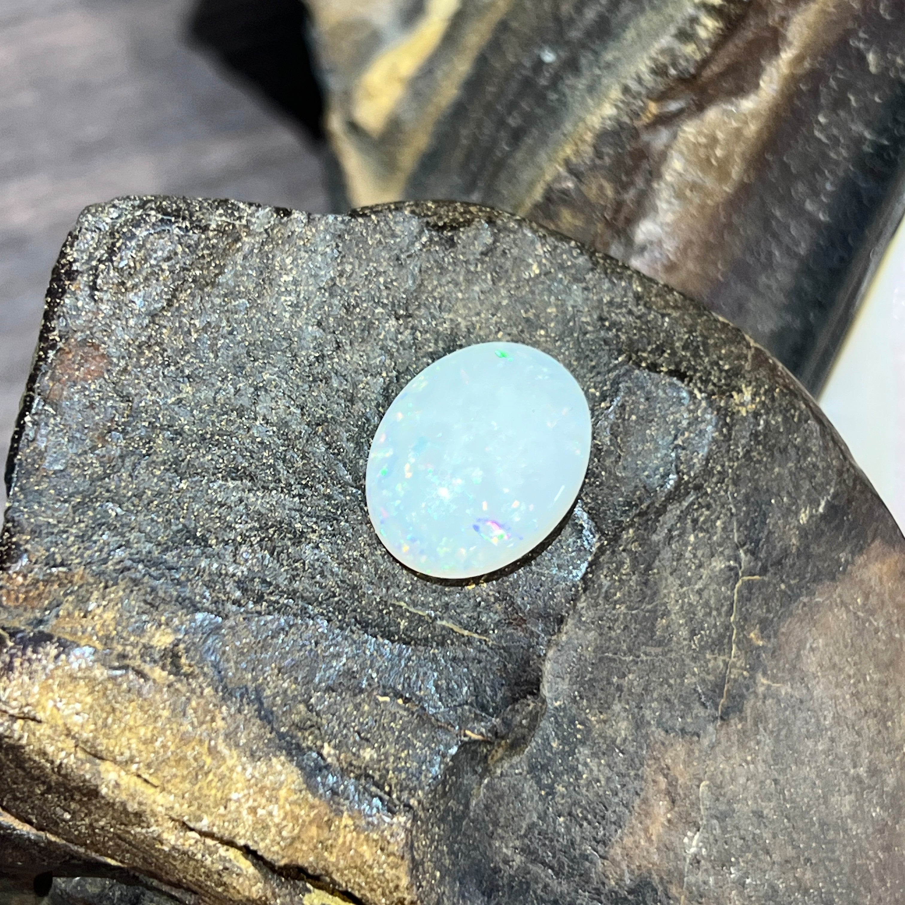 Upright view of the 16x12mm white opal oval, blue-green sparkle across its face