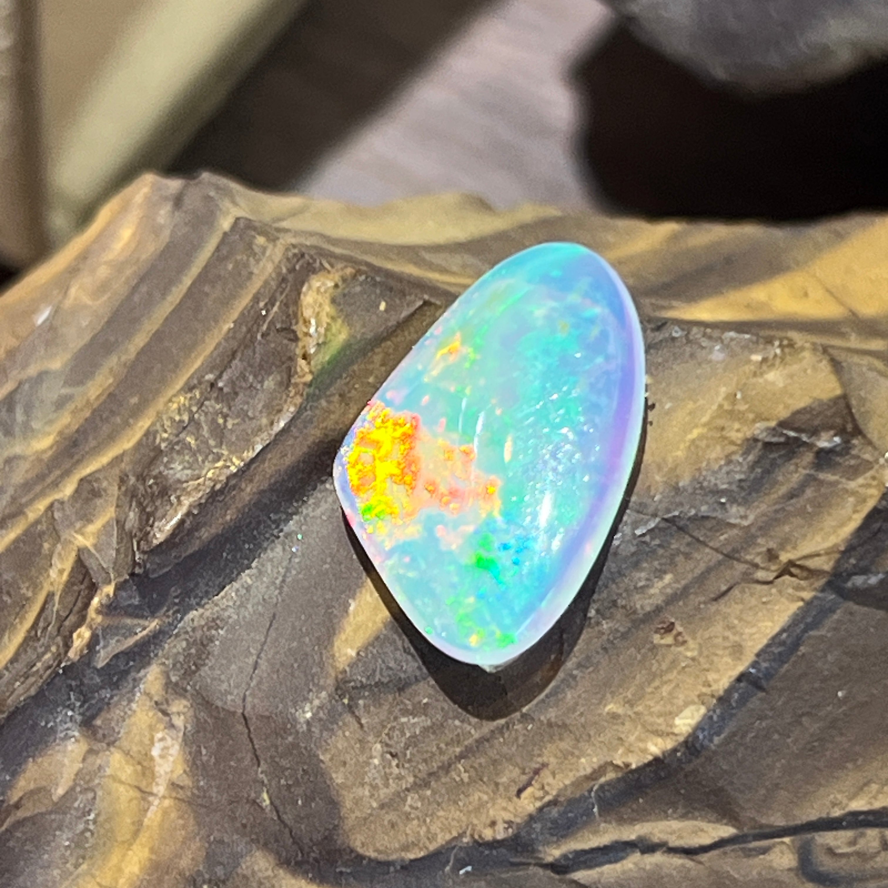 Australian crystal opal tilted in sunlight, bright orange and yellow play of colour across the top