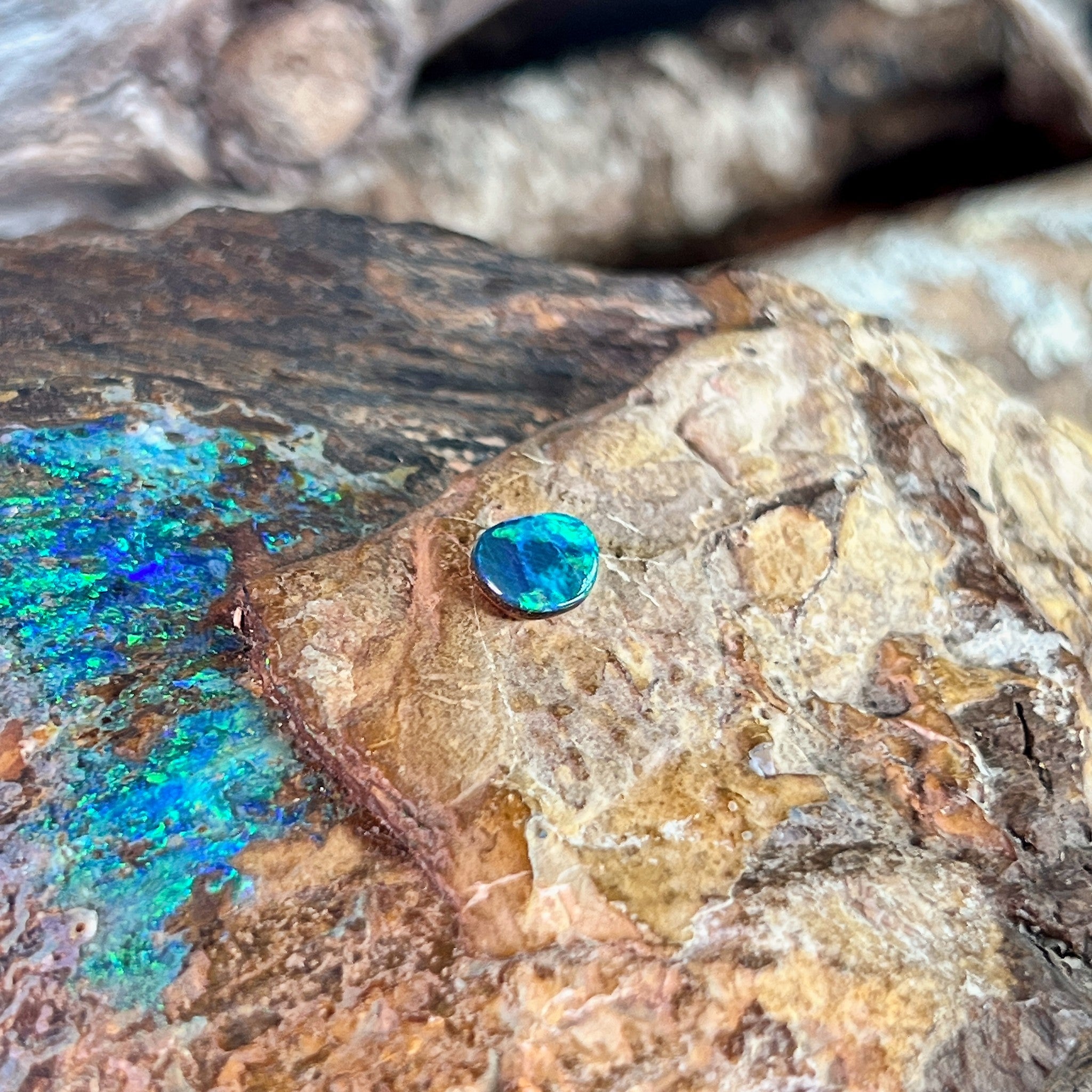 Freeform 0.65ct Australian opal doublet glowing blue against pale ironstone
