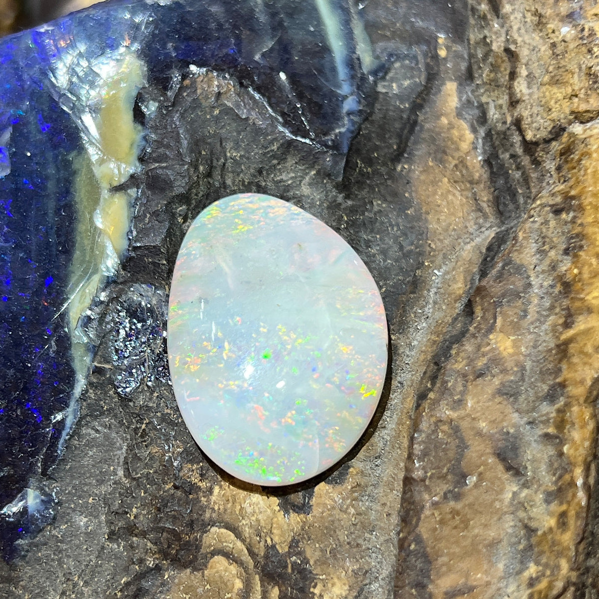 Australian white opal 14.70ct freeform cabochon, 28x19.4mm, yellow, orange and green with white zones, loose and unset, on rock