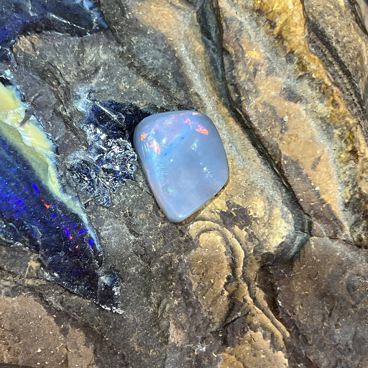 6.30ct freeform black opal loose stone, red, orange, green and blue play-of-colour, unset, on rock
