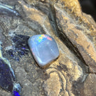 Australian black opal 6.30ct freeform cabochon, 18.3x14.4mm, red, orange and green with a blue zone, loose and unset, on rock