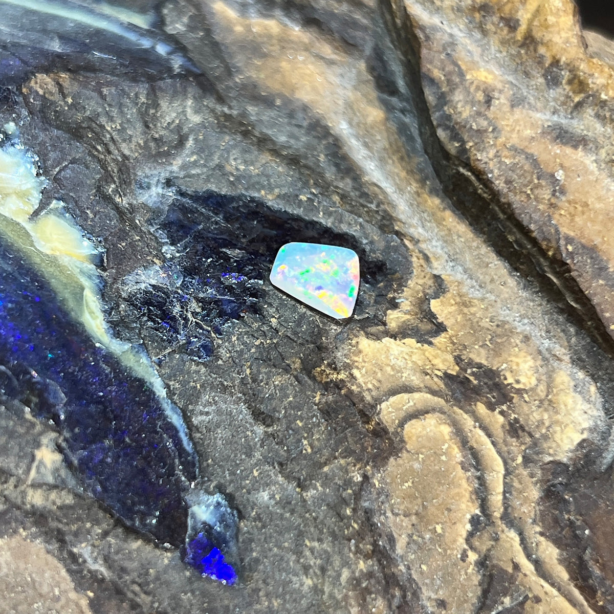 0.65ct freeform crystal opal loose stone, red, orange and green play-of-colour, unset, on rock