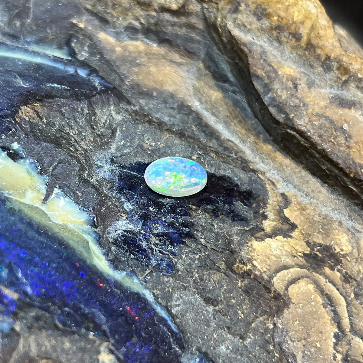 1.00ct oval crystal opal loose stone, red, orange and green play-of-colour, unset, on rock