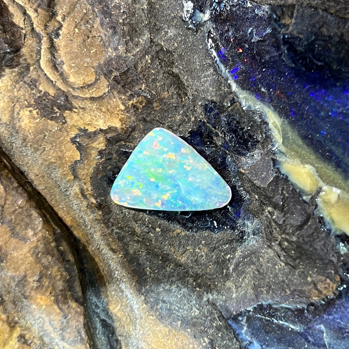 2.15ct triangular crystal opal loose stone, yellow, orange, green and blue play-of-colour, unset, on rock