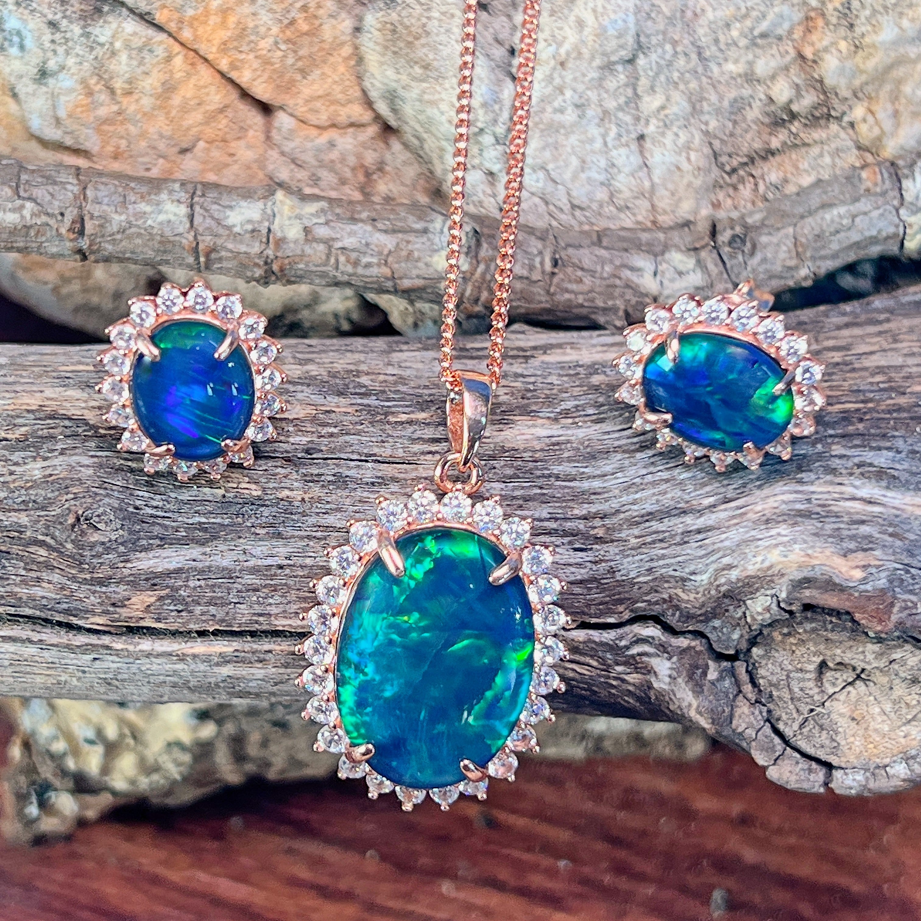 Halo-set opal triplet jewellery set in rose gold-plated silver, viewed on driftwood