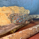Wide sterling silver Australian opal inlay bangle resting on driftwood