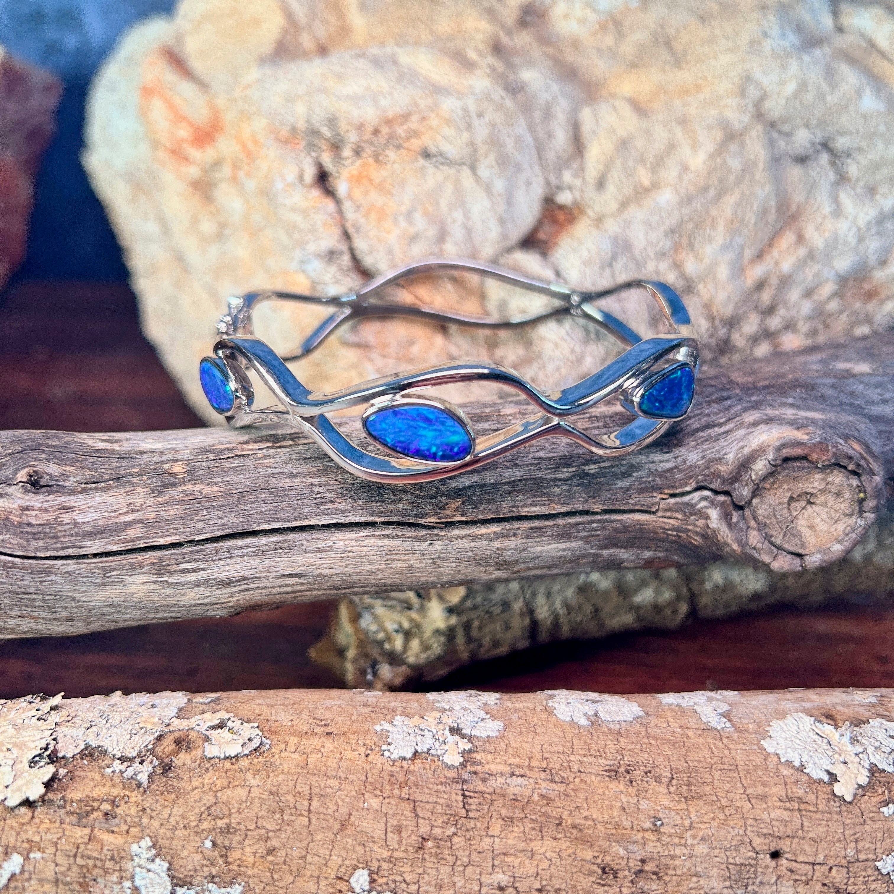 Sterling silver opal doublet bangle resting on weathered driftwood, blue and green play-of-colour