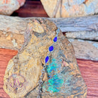 Sterling silver bracelet with three opal doublets resting on rough rock streaked with green and blue