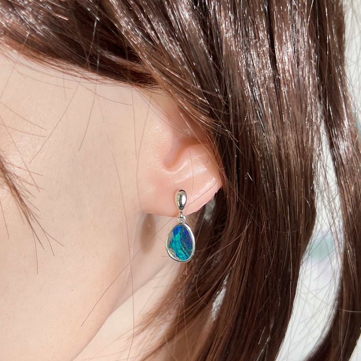 Australian opal doublet earrings worn on the ear, blue, green and pink play-of-colour