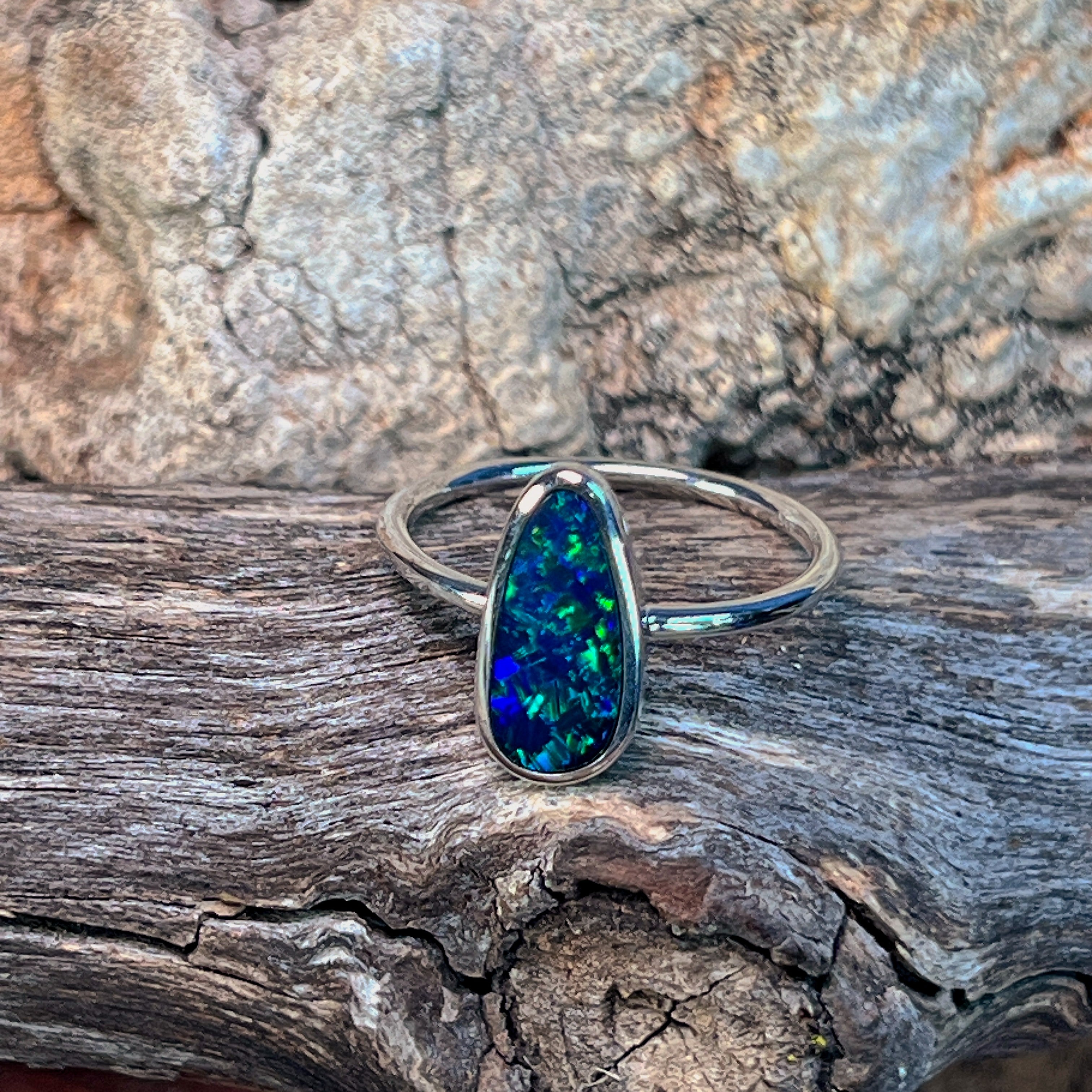 Sterling silver freeform opal doublet solitaire ring angled on driftwood