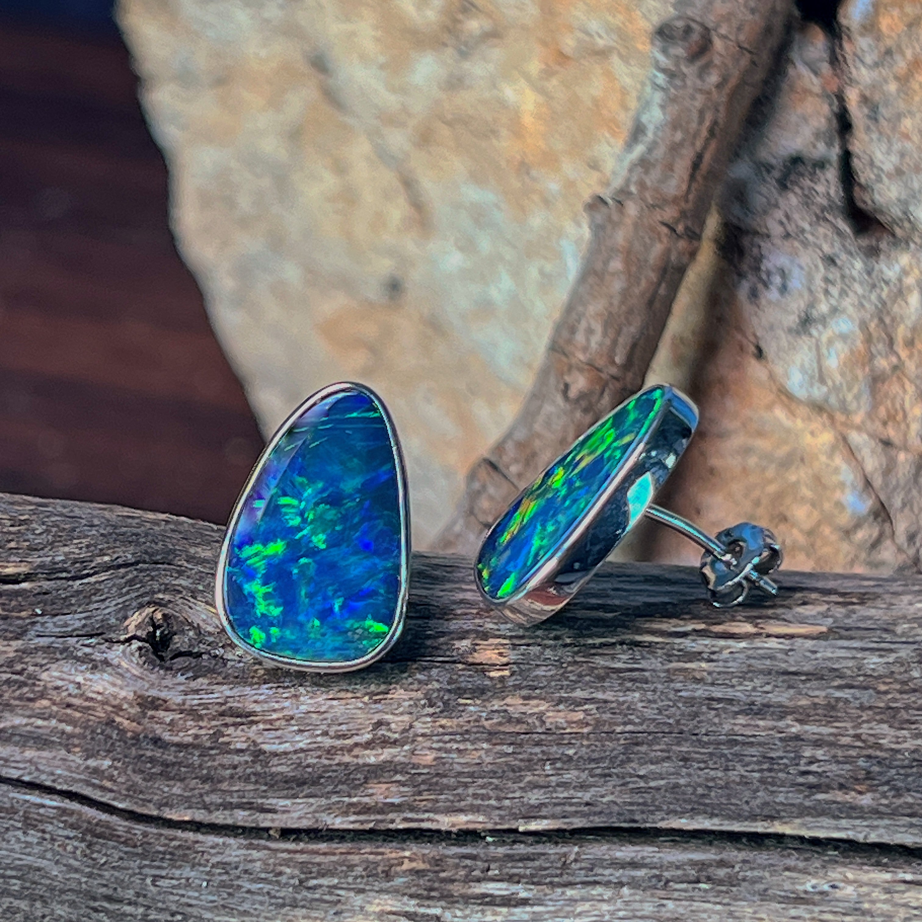 Freeform opal doublet stud earrings in sterling silver resting on weathered driftwood