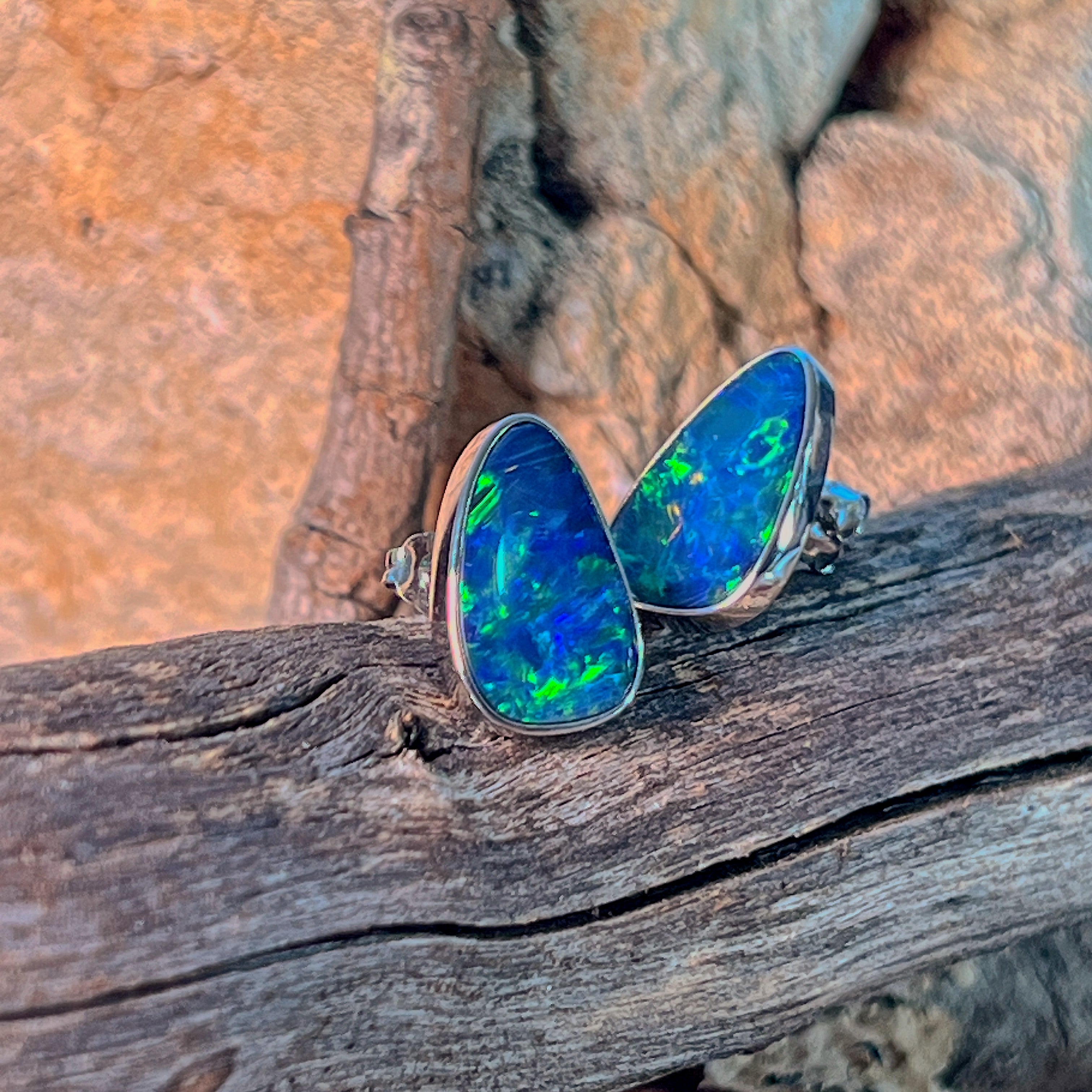 Pair of freeform opal doublet stud earrings in silver, viewed from above on driftwood