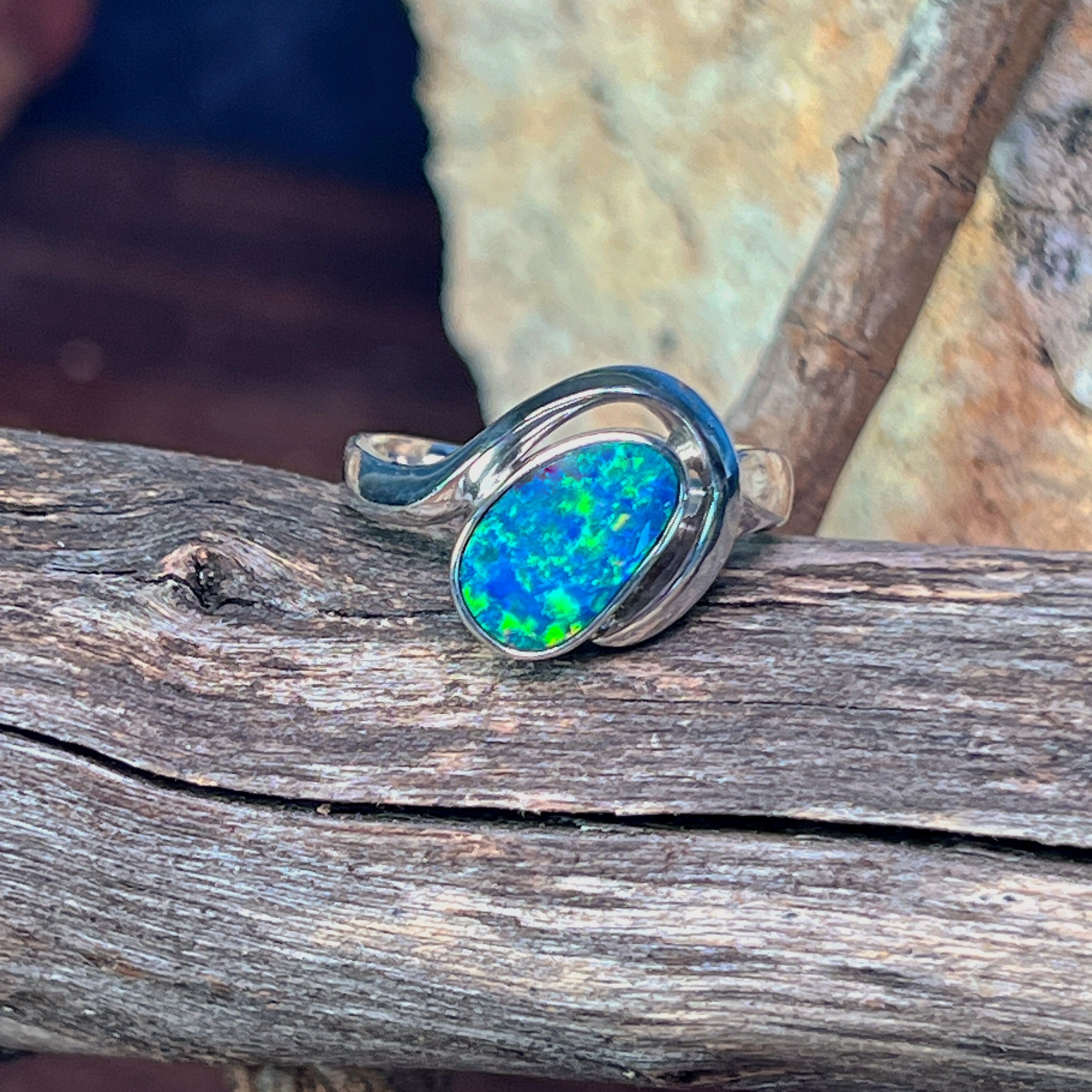 Silver bypass ring with oval opal doublet resting on weathered driftwood