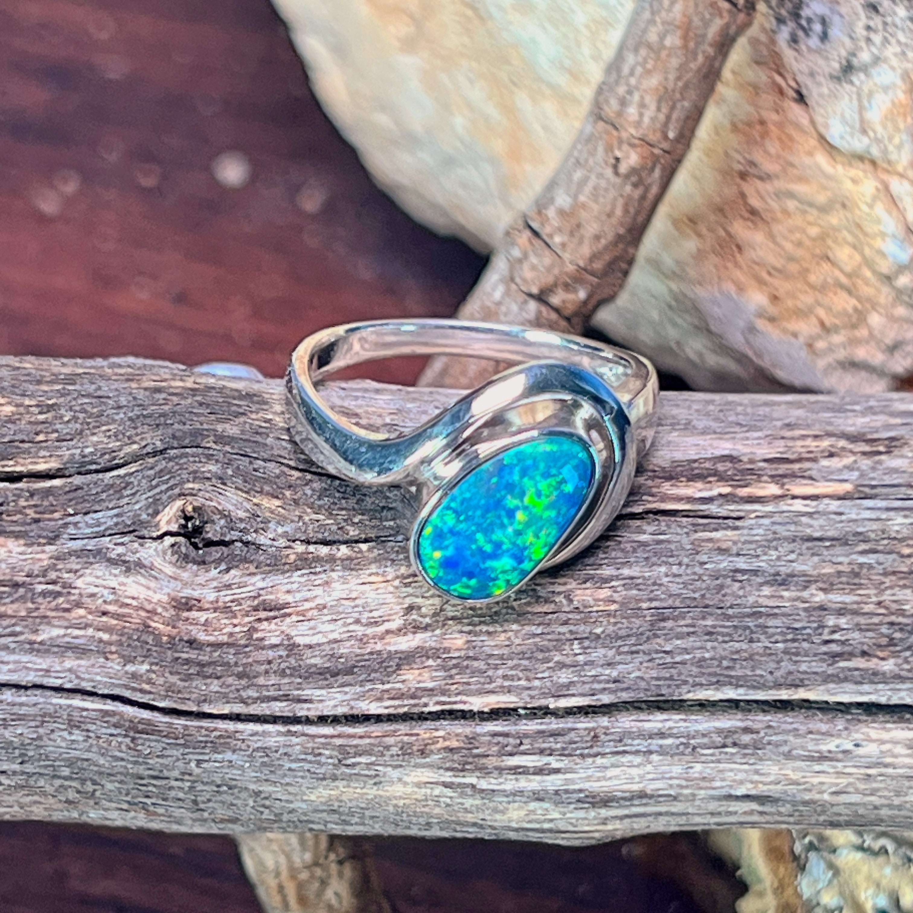 Sterling silver bypass solitaire ring with opal doublet angled against driftwood