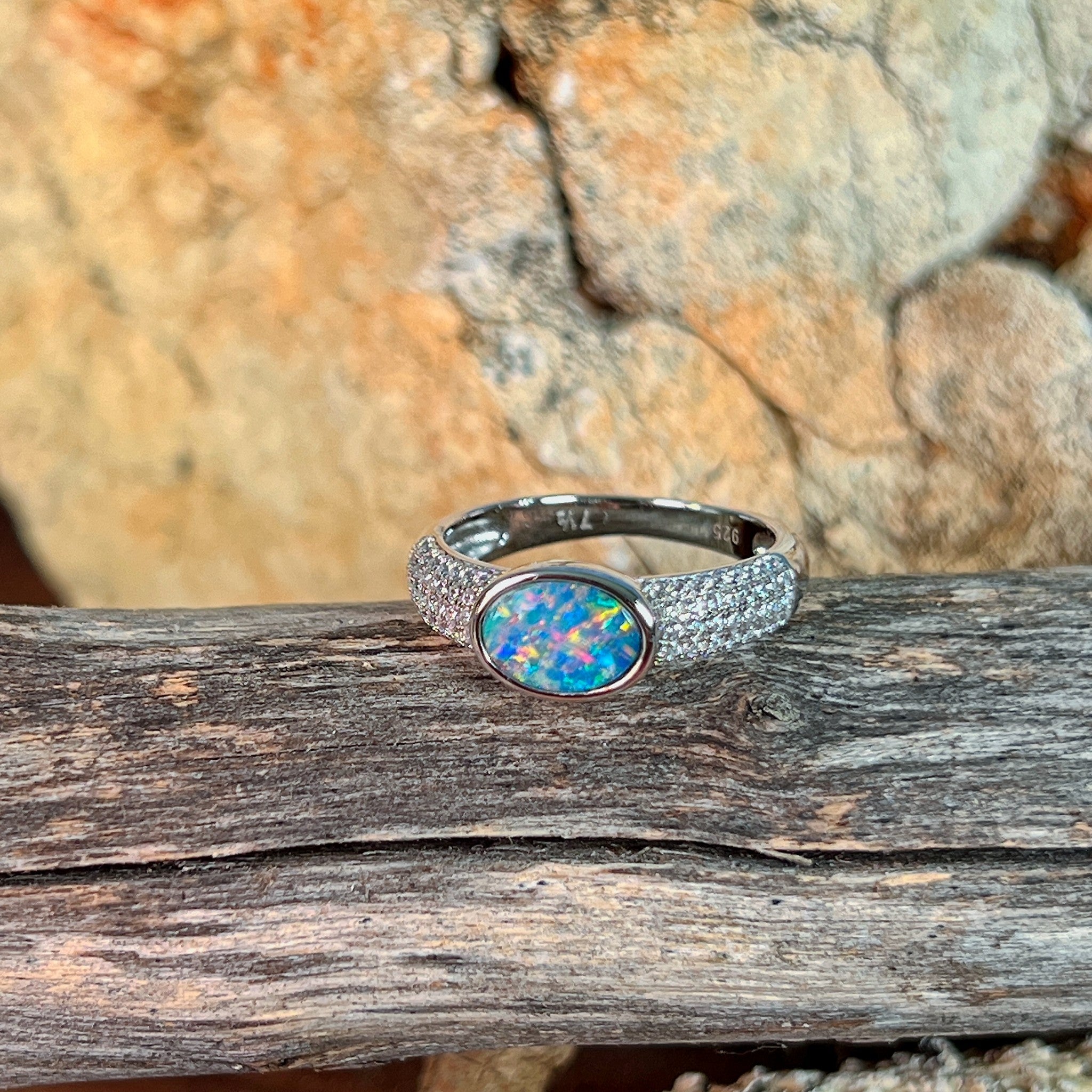 Oval opal doublet ring on a pave silver band resting on weathered driftwood