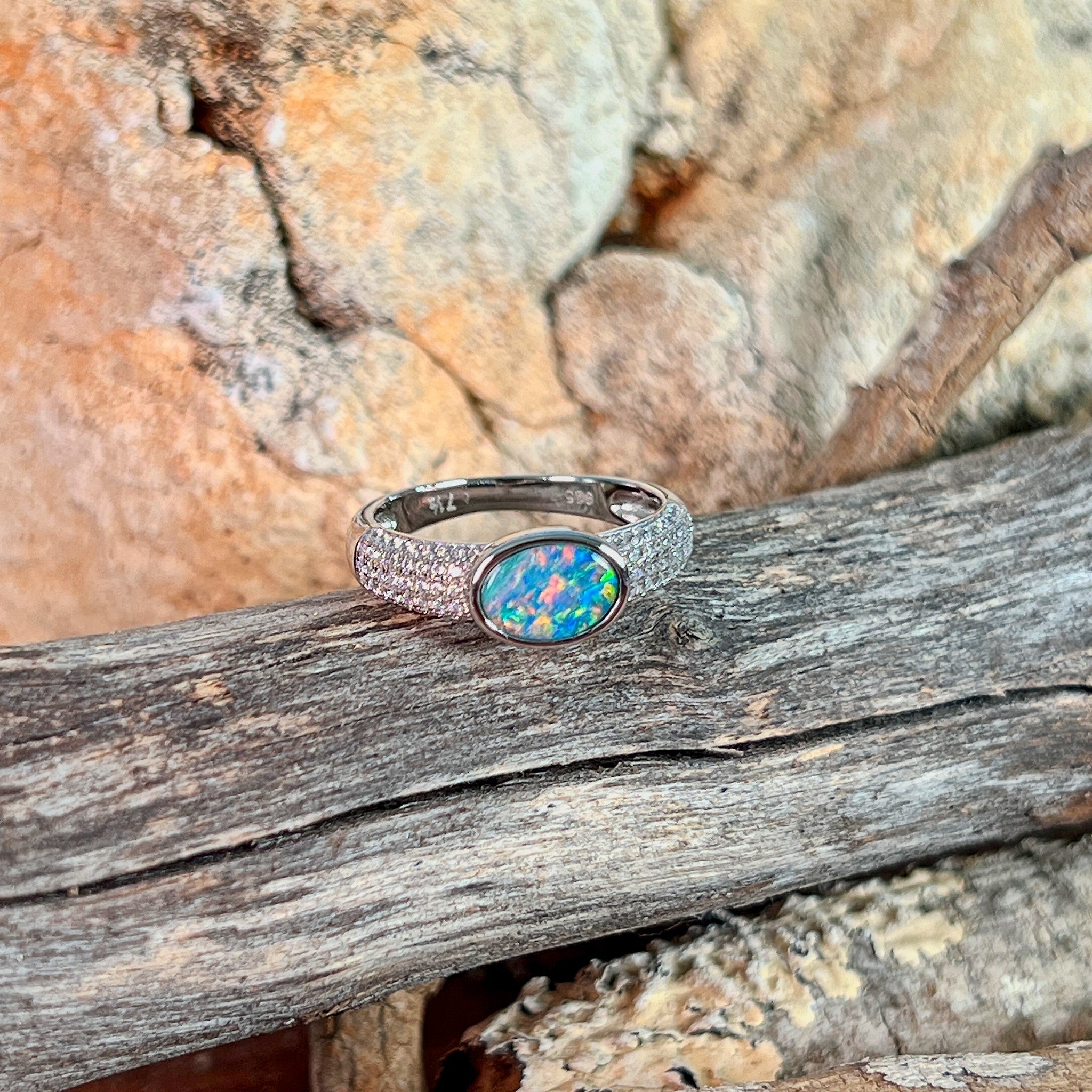 Oval opal doublet ring on a pave silver band on driftwood against Australian sandstone
