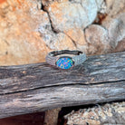 Oval opal doublet ring on a pave silver band photographed in profile on driftwood, showing the setting