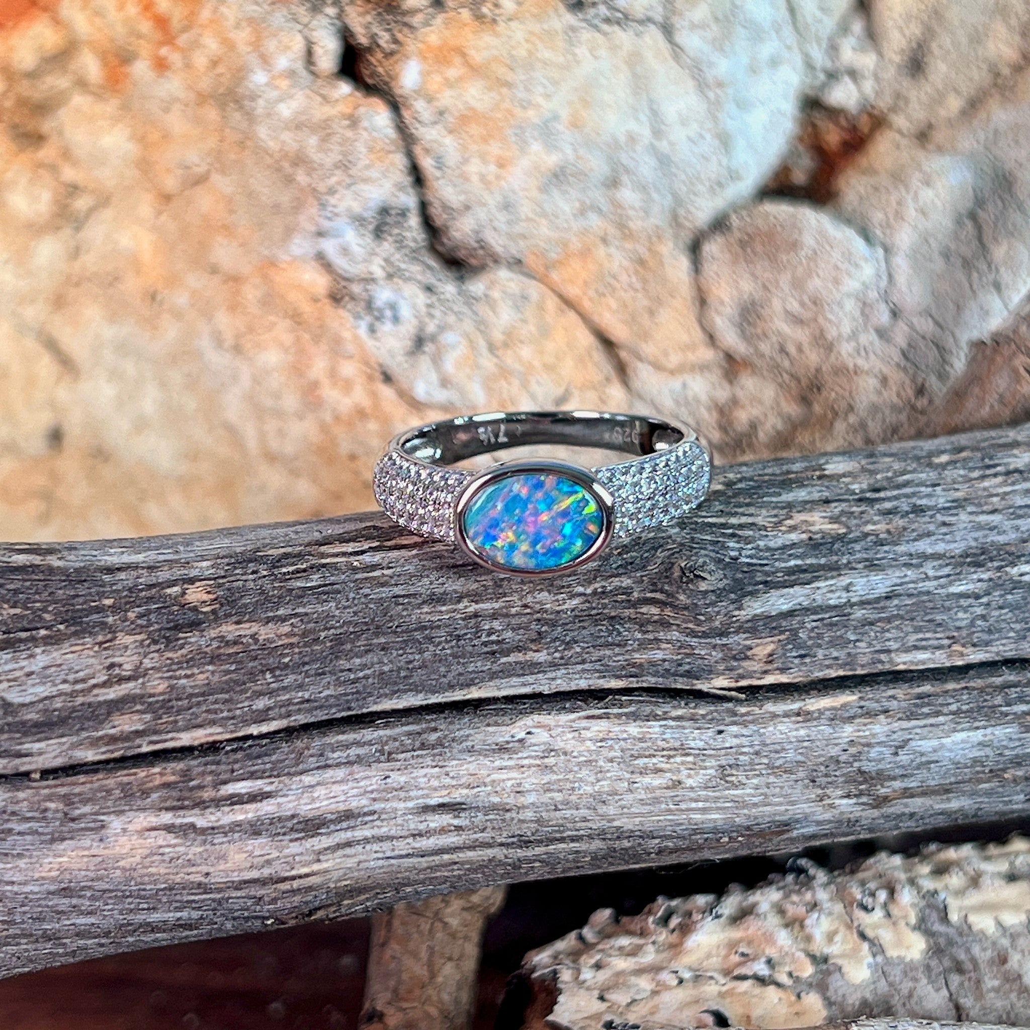 Oval opal doublet ring on a pave silver band photographed in profile on driftwood, showing the setting