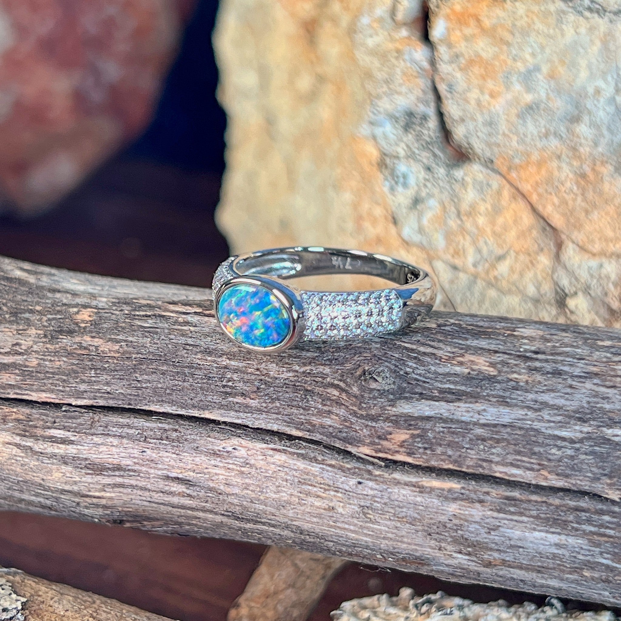 Oval opal doublet ring on a pave silver band on driftwood, the oval opal doublet catching the light