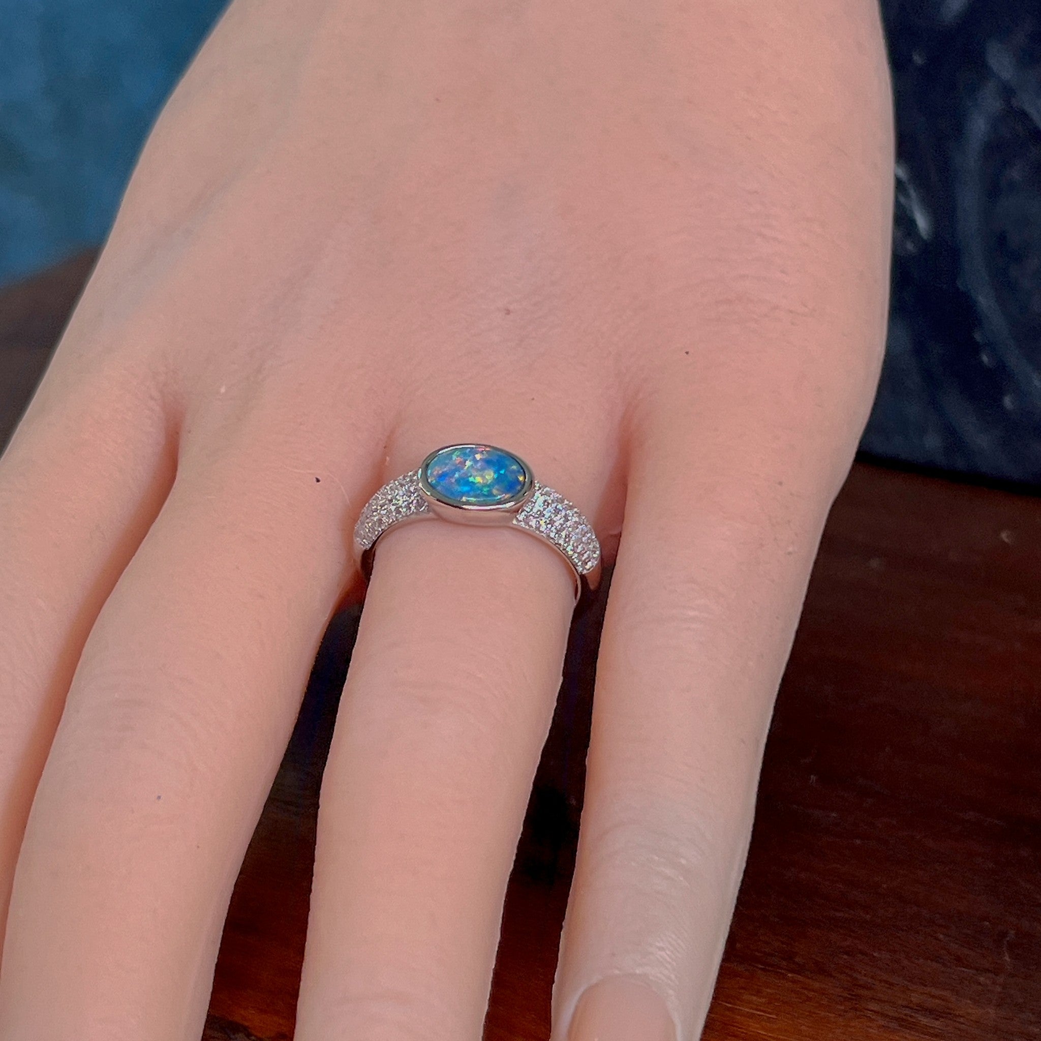 Oval opal doublet ring on a pave silver band on the hand, angled to catch the blue, red and green play of colour