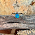 Oval opal doublet ring with zirconia shoulders resting on weathered driftwood
