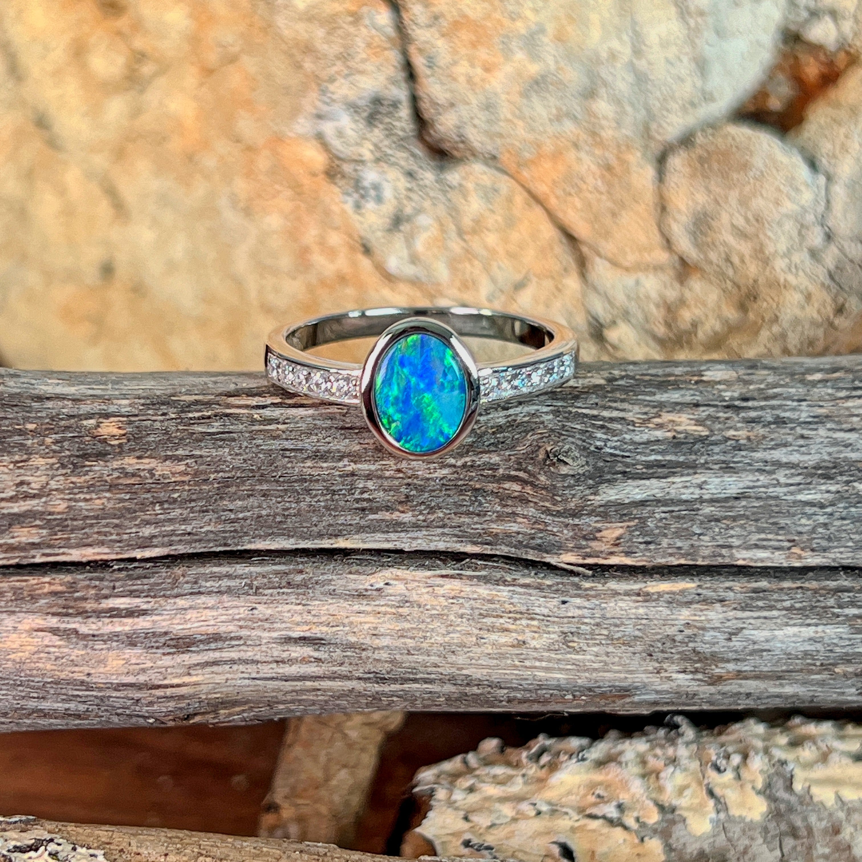 Oval opal doublet ring with zirconia shoulders resting on weathered driftwood