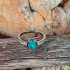 Oval opal doublet ring with zirconia shoulders photographed in profile on driftwood, showing the setting
