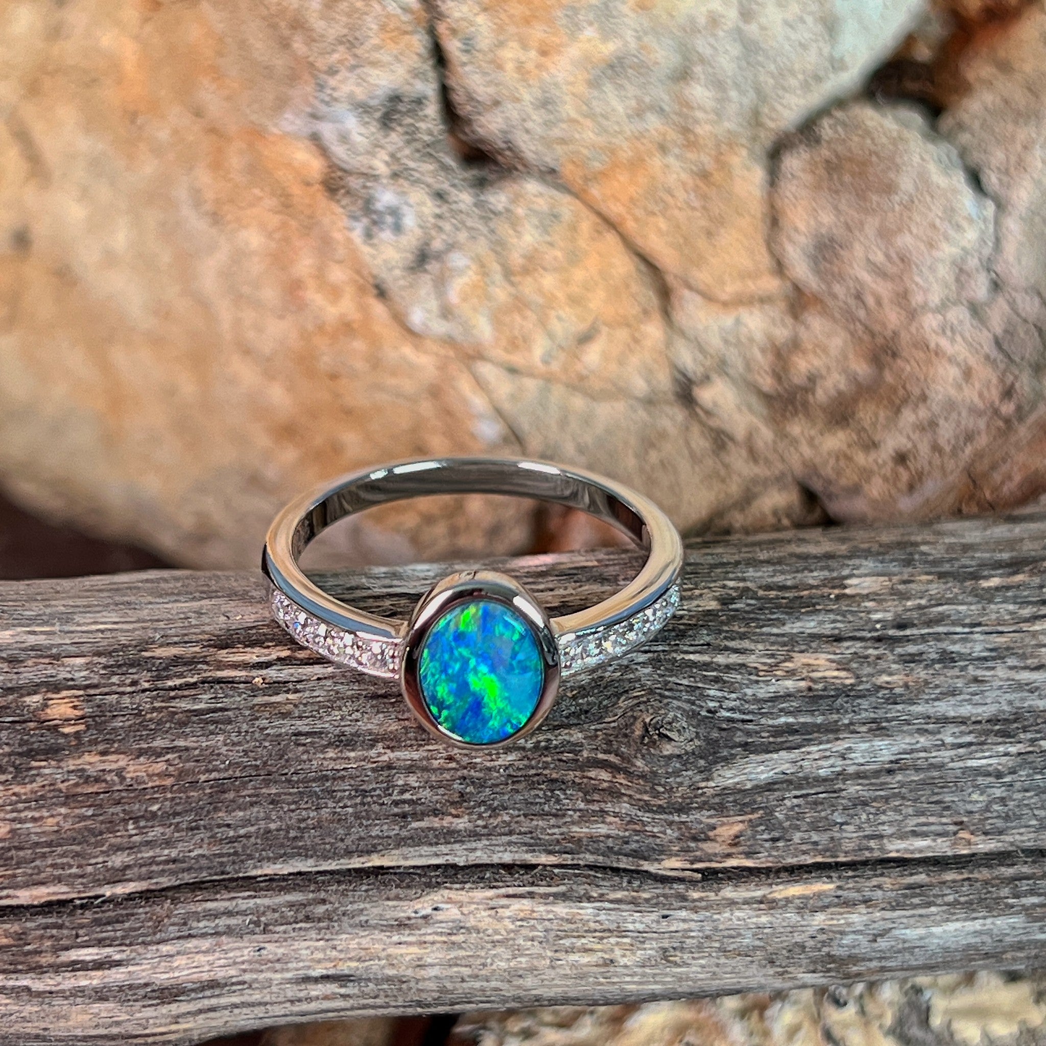 Oval opal doublet ring with zirconia shoulders photographed in profile on driftwood, showing the setting