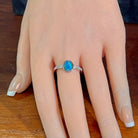 Oval opal doublet ring with zirconia shoulders worn on the hand, viewed across the fingers