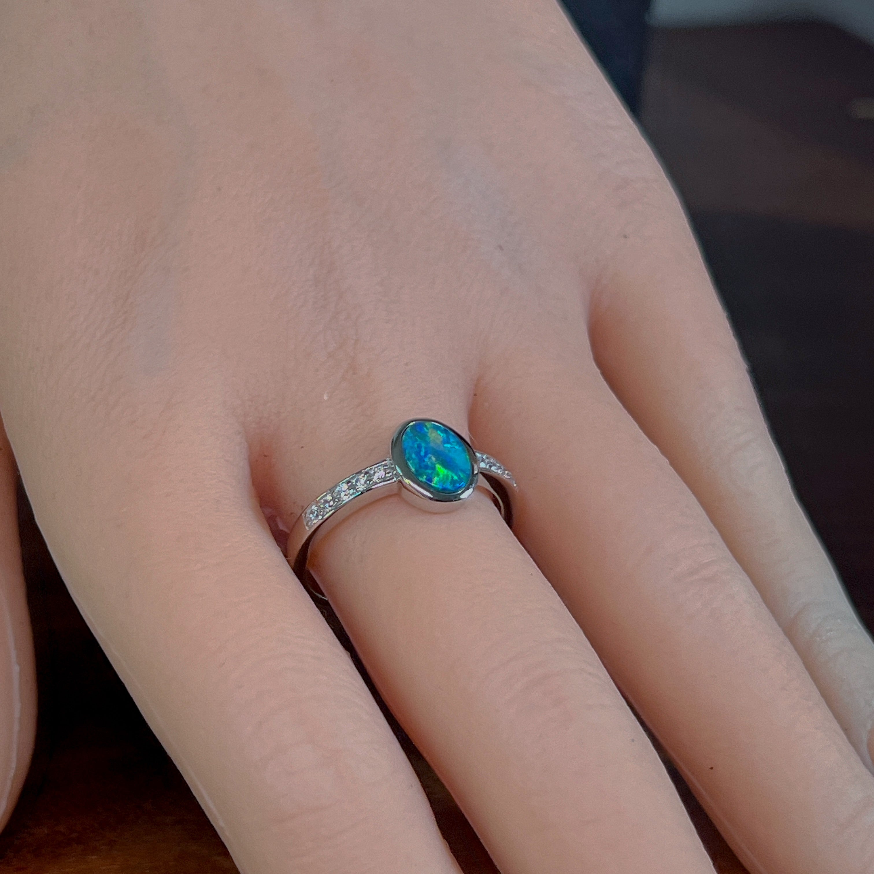 Oval opal doublet ring with zirconia shoulders worn on the hand, showing its scale on the finger