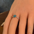 Oval opal doublet ring with zirconia shoulders on the hand, angled to catch the blue, red and green play of colour