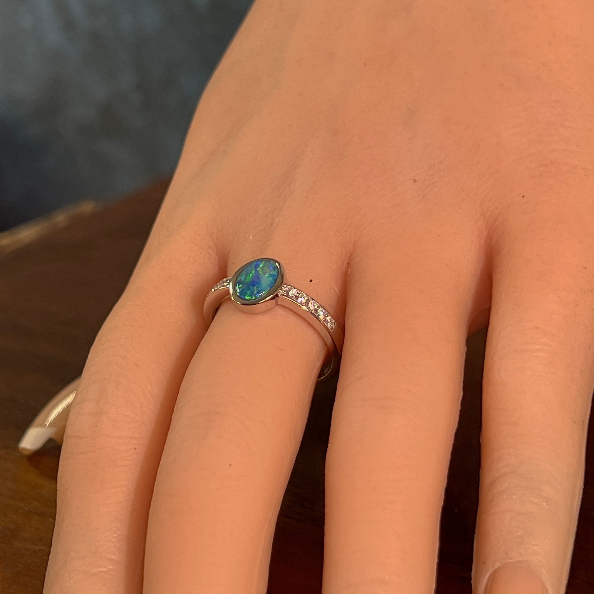 Oval opal doublet ring with zirconia shoulders on the hand, angled to catch the blue, red and green play of colour