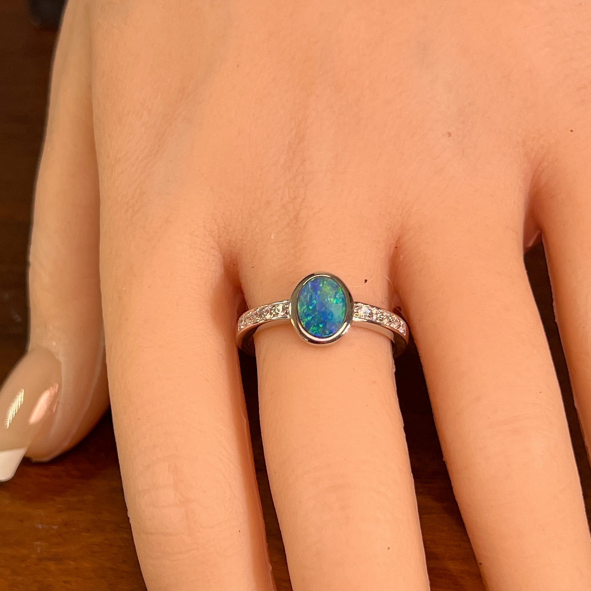Oval opal doublet ring with zirconia shoulders worn on the hand, full view across the fingers